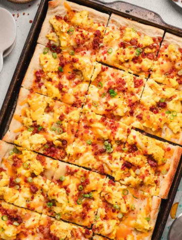 breakfast pizza in a baking sheet topped with scrambled eggs and bacon and cheese